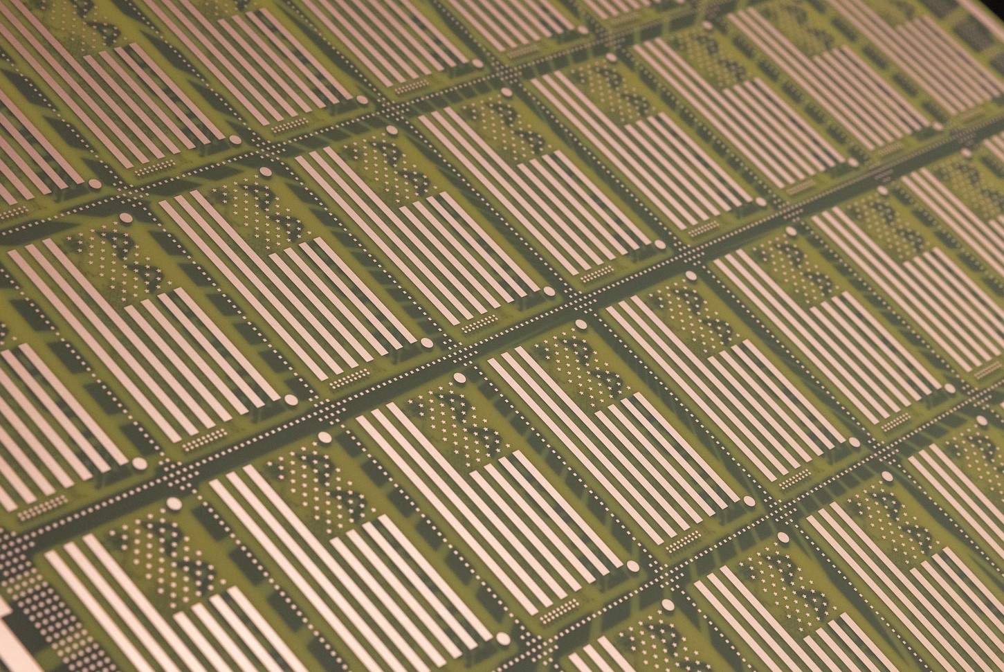 Close-up of a circuit board showcasing the intricate grid pattern typical of American PCB manufacturing, with green and metallic elements. Rows of horizontal lines and small circles form a detailed, repetitive electronic design emblematic of sophisticated PCBAA standards.