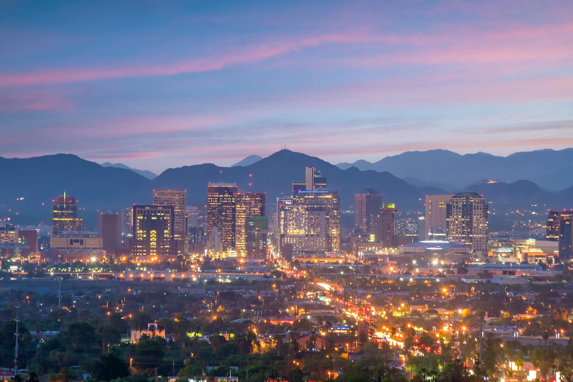 A city skyline at dusk with illuminated buildings and silhouetted mountains under a colorful sky transitioning from pink to blue, reminiscent of Arizonas horizons. The vibrant glow hints at its expanding manufacturing, where microelectronics manufacturing plays a pivotal role in the urban landscape.