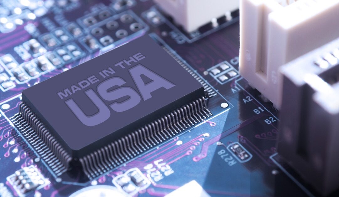 Close-up of a computer motherboard with a black chip labeled Made in the USA in bold text, placed centrally. The board features various electronic components and a purple-toned circuit board.